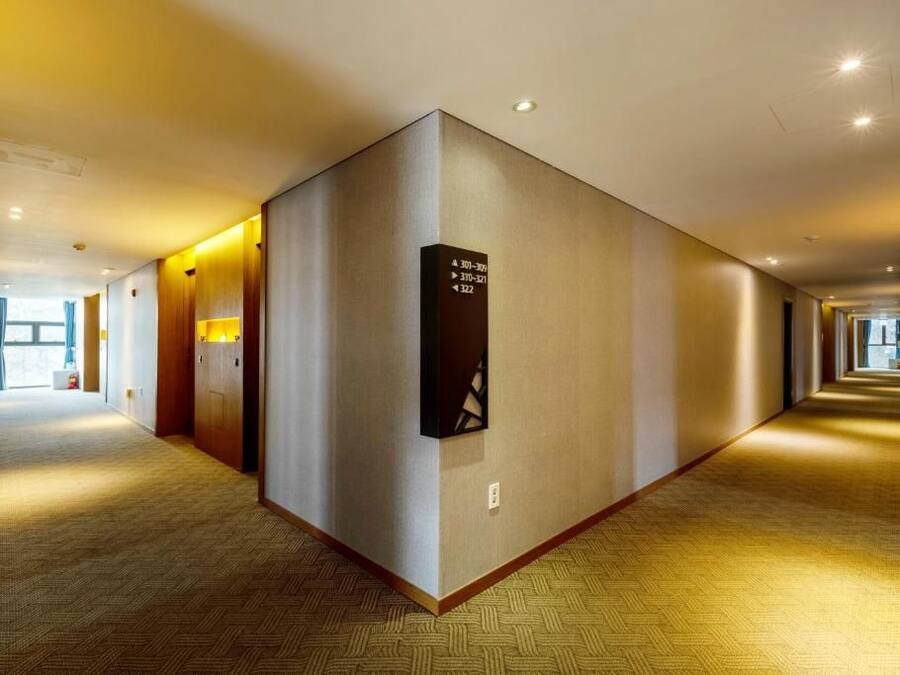 Un pasillo de hotel con piso alfombrado, un directorio en la pared y una puerta a la izquierda.