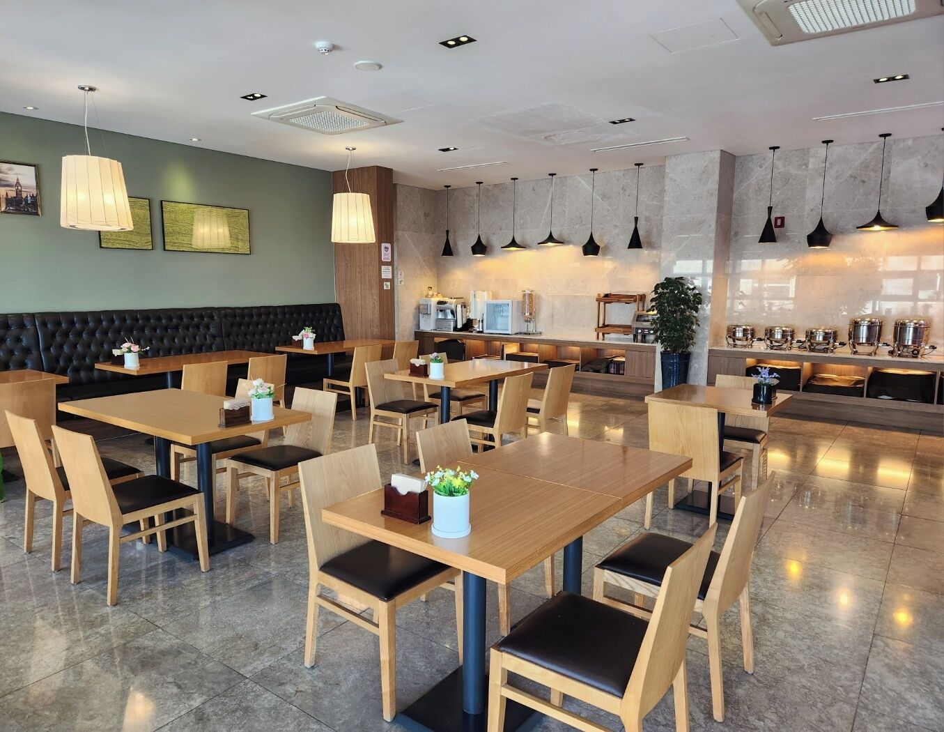 A modern restaurant with wooden tables and chairs, a bar area, and pendant lighting.