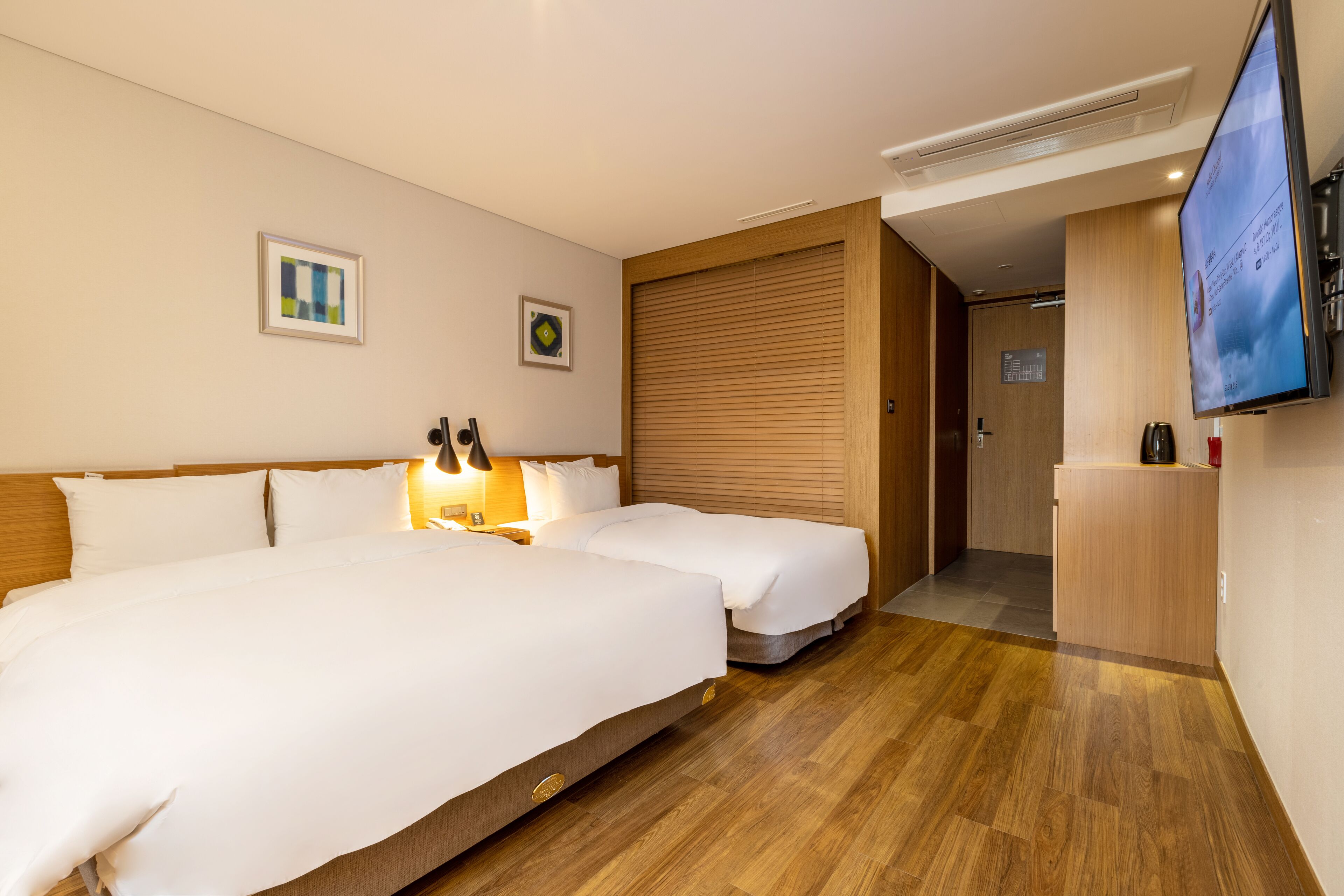 Habitación de hotel con dos camas, un televisor y piso de madera.