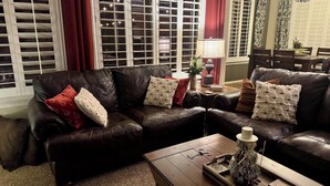 Een woonkamer met een donker leren bank, een houten salontafel en een rood gordijn.