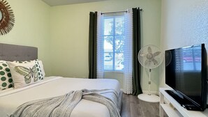 A bedroom with a bed, a TV on a stand, a ceiling light, and a window with curtains. - Private Studio 4 minutes from Strip !!! (Las Vegas)