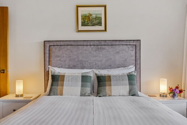 A neatly made bed with a striped duvet, two bedside tables with lamps, and a framed picture on the wall.