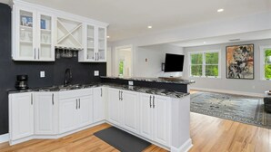 A modern kitchen with white cabinetry, a black countertop, and a black rug. - Private Luxury Stay in Expansive Home & Property (EASTON)