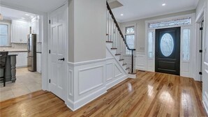 A spacious kitchen with white cabinetry, a wooden floor, and a staircase leading to a dark door with a circular window. - Private Luxury Stay in Expansive Home & Property (EASTON)