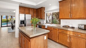 A modern kitchen with wooden cabinets, granite countertops, a stainless steel refrigerator, and a view of a swimming pool. - Everything you want! Pool/spa, Golf Course, Mountain Views (Palm Desert)