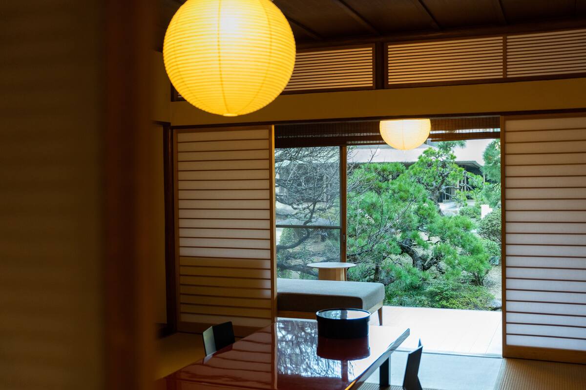 A traditional Japanese room with tatami flooring, a low table, and a view of a garden through sliding doors.
