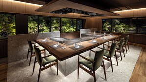 A modern dining area with a long table, chairs, and a central island with a built-in stove. - Suisui Garden Ryokan (Kitakyushu)