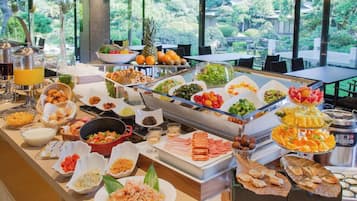 A buffet with various food items and a view of a garden through large windows.