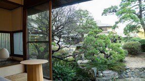 A traditional Japanese room with tatami flooring, a low wooden table, and a view of a garden with a pond and trees. - Suisui Garden Ryokan (Kitakyushu)