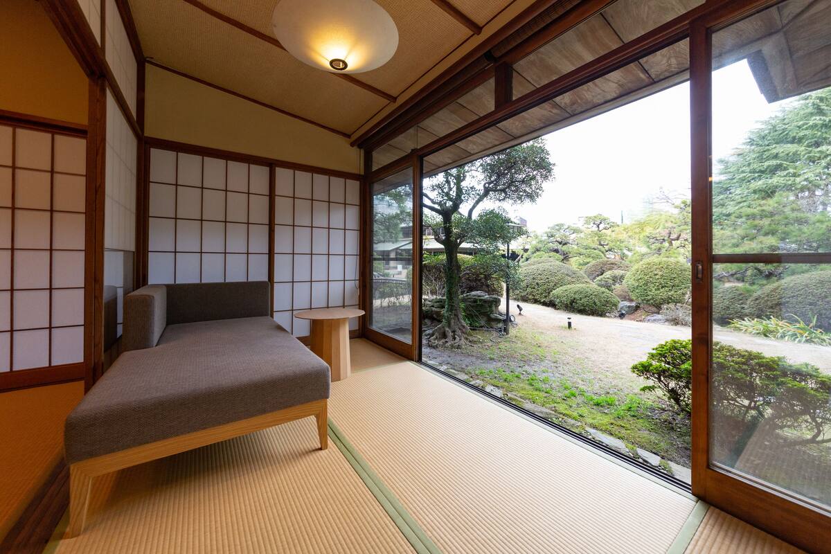A traditional Japanese room with tatami flooring, a low wooden bed, and a sliding door leading to a garden.