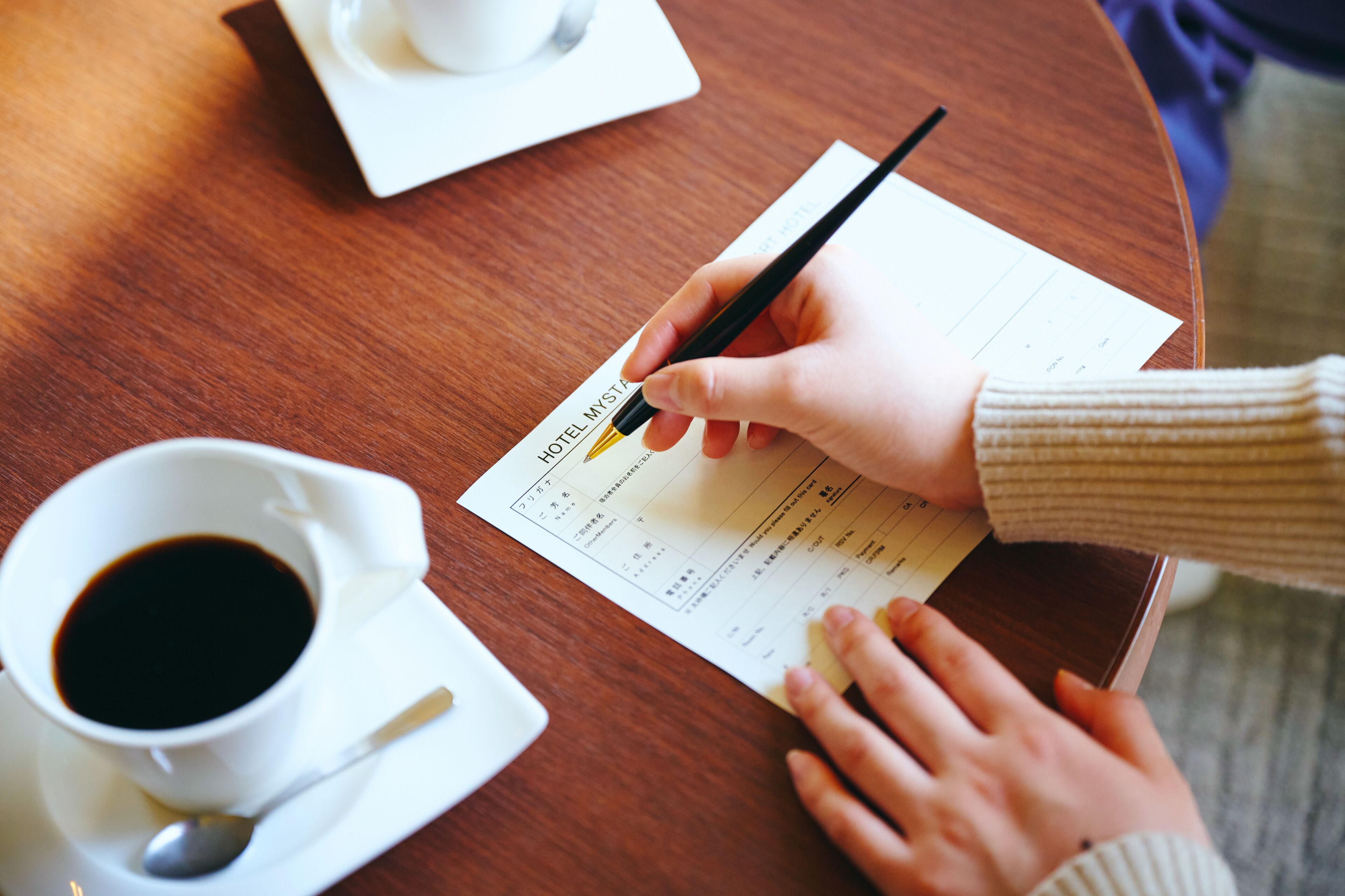 Una persona escribe en un recibo de hotel con una taza de café sobre la mesa.