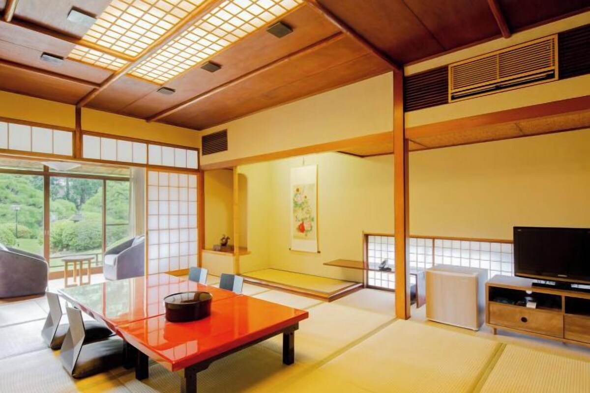 A traditional Japanese room with tatami flooring, a low table, a television, and a sliding door leading to a balcony.