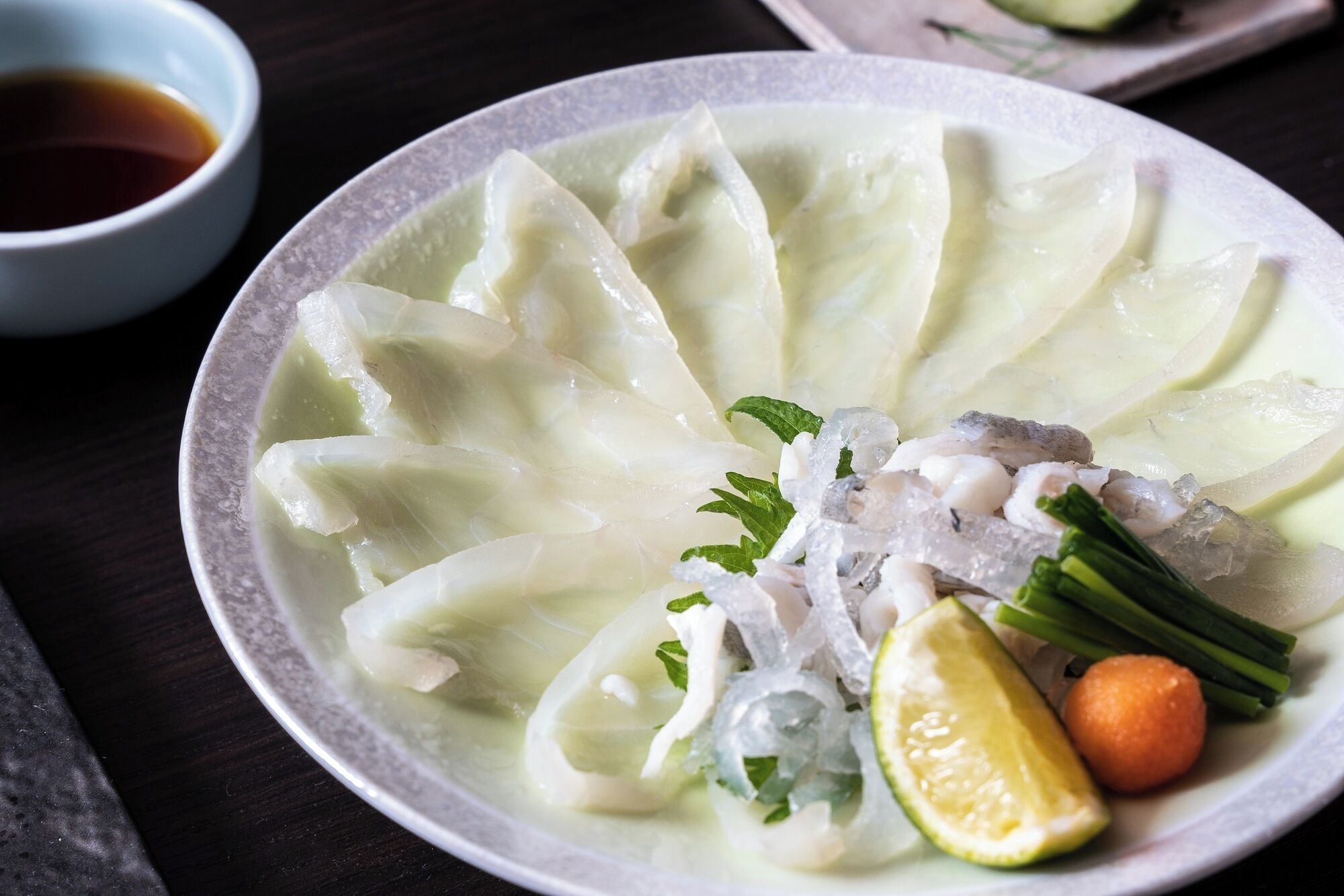 A bowl of clear soup with noodles, fish, lime, and herbs.