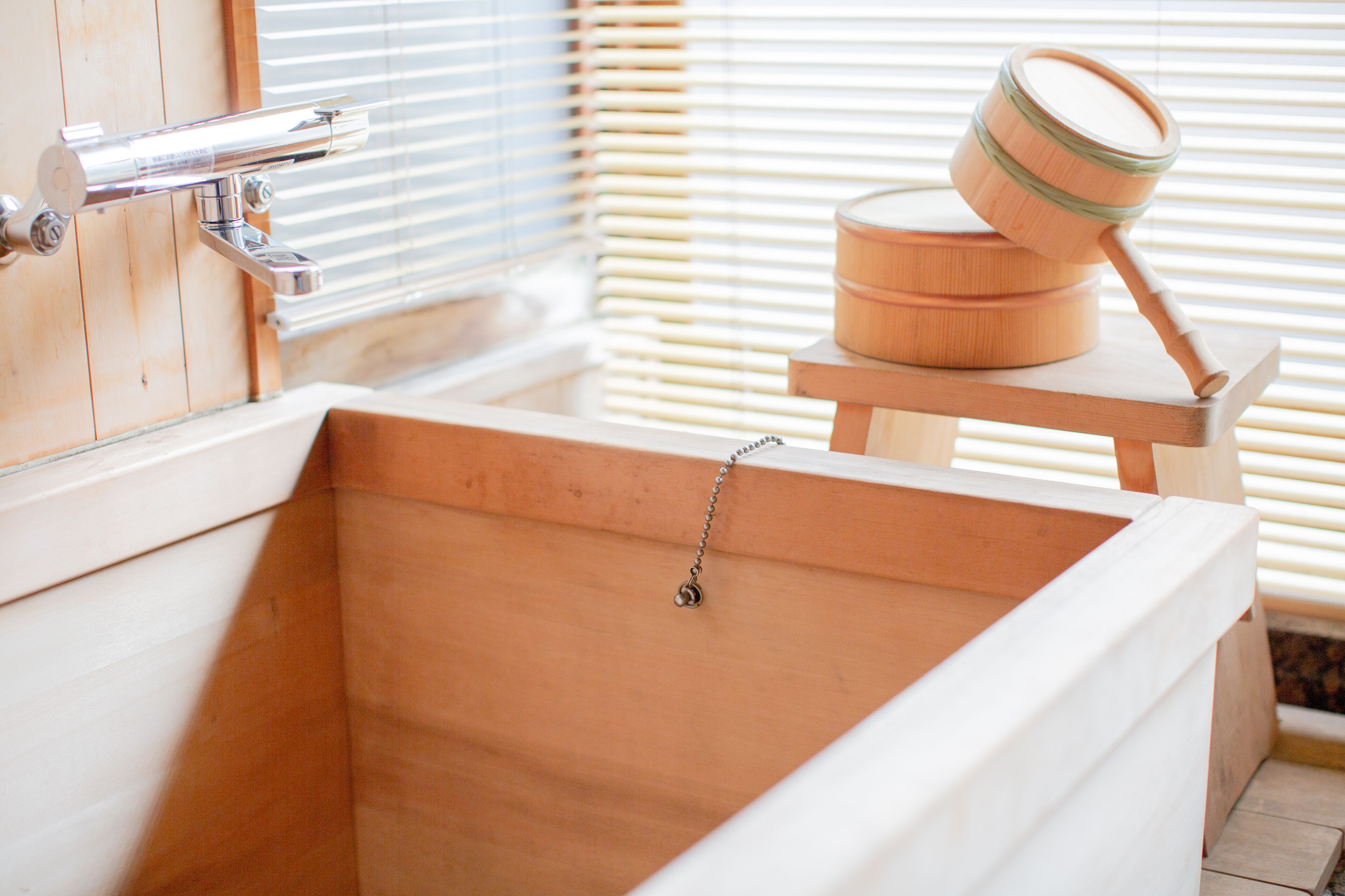 A wooden bathtub with a faucet and a wooden container on a wooden stool.