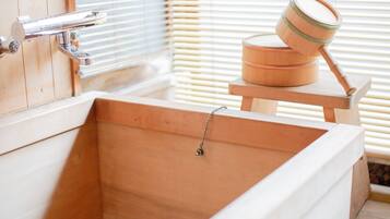 A wooden bathtub with a faucet and a wooden container on a wooden stool.