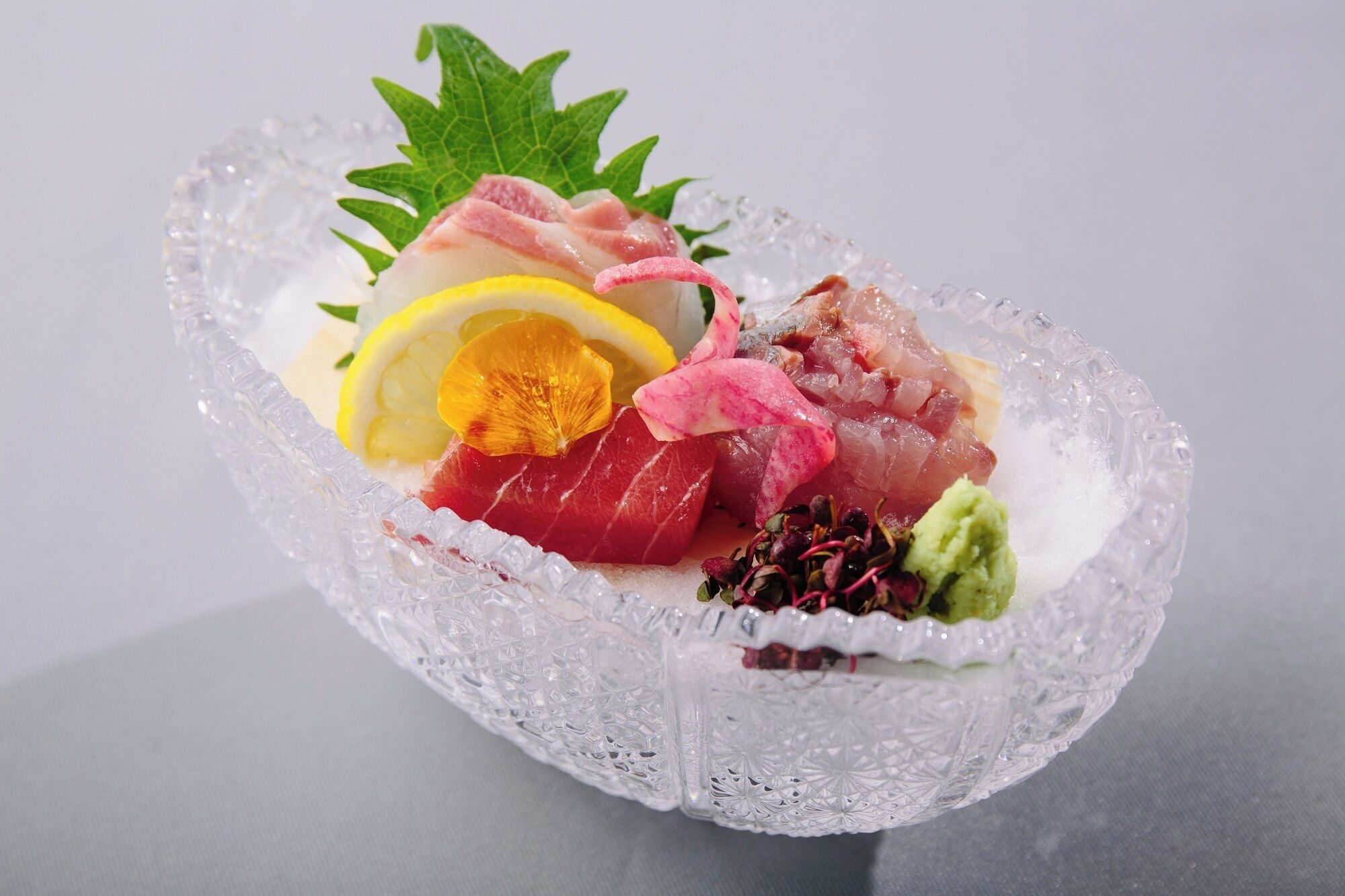 A clear glass bowl with various types of sashimi arranged on a bed of ice.