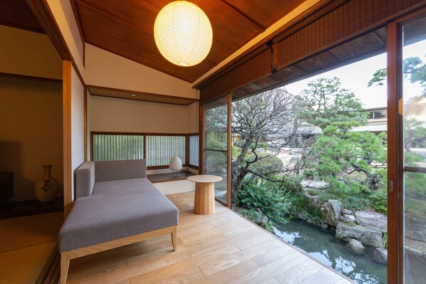 A modern room with a wooden floor, a bed, a small round table, and a view of a garden through large windows. - Suisui Garden Ryokan (Kitakyushu)