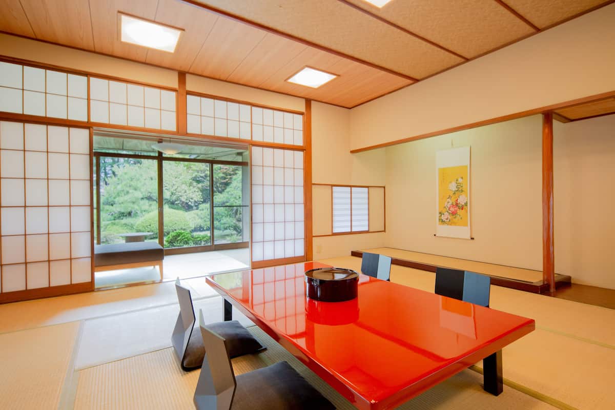 A traditional Japanese room with tatami flooring, a sliding door leading to a garden, and a red lacquered table.