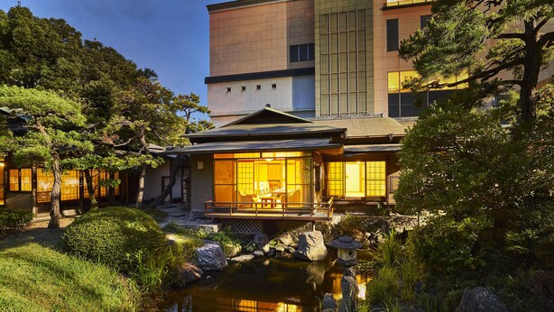 A traditional Japanese-style building with a koi pond, wooden bridge, and surrounding greenery. - Suisui Garden Ryokan (Kitakyushu)