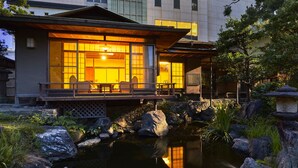 A traditional Japanese-style building with a koi pond in front, wooden deck, and large windows. - Suisui Garden Ryokan (Kitakyushu)