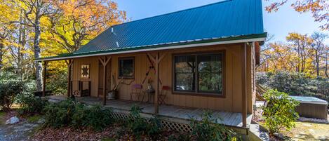 A wooden cabin with a blue roof, a porch with chairs, and a hot tub.
