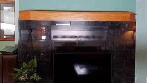 Una chimenea con un cuadro enmarcado encima, una planta en maceta a la izquierda y un fuste de madera.