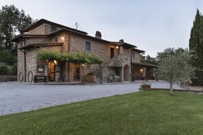 Traditional stone building with a symmetrical facade and central entrance, set amidst a well-maintained lawn.