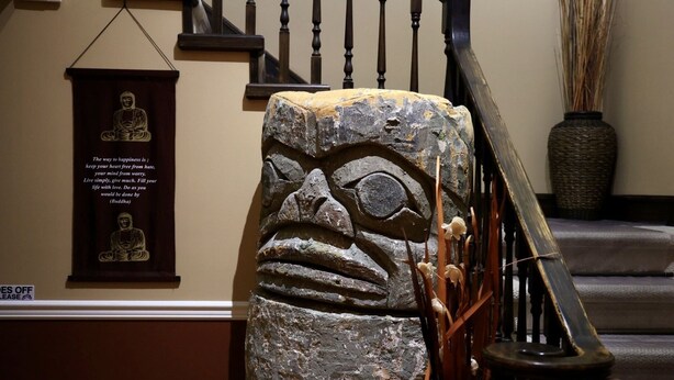 A stone sculpture of a face with a sign that says "SHOES OFF PLEASE" on a staircase railing. - 🔳 48% discount • Steam Shower • 9 mins @ Airport  (Richmond)