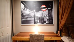 A dining area with a wooden table and a woven chair, a framed black and white photo of a city street above the table, and a curtain on the right. - 🔳 48% discount • Steam Shower • 9 mins @ Airport  (Richmond)