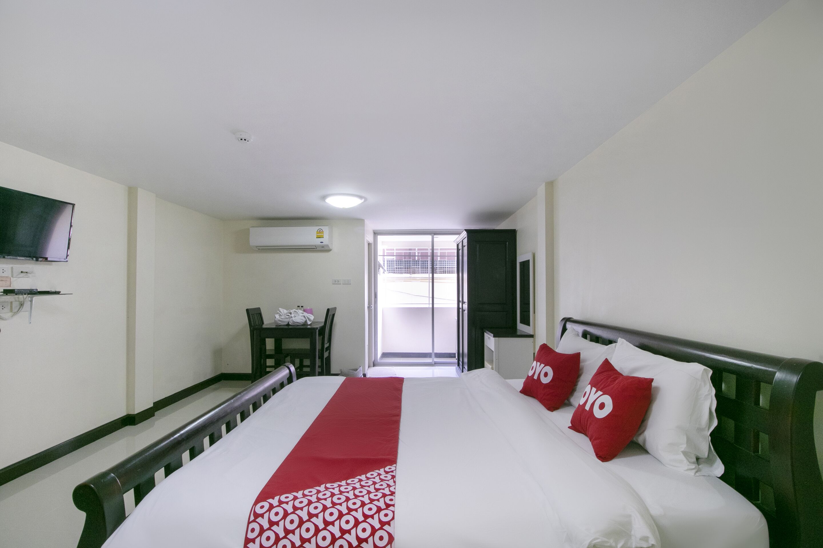 A hotel room with a bed, a TV mounted on the wall, a desk with a chair, and a window with a view of the outside.