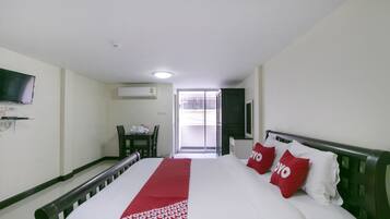 A hotel room with a bed, a TV mounted on the wall, a desk with a chair, and a window with a view of the outside.
