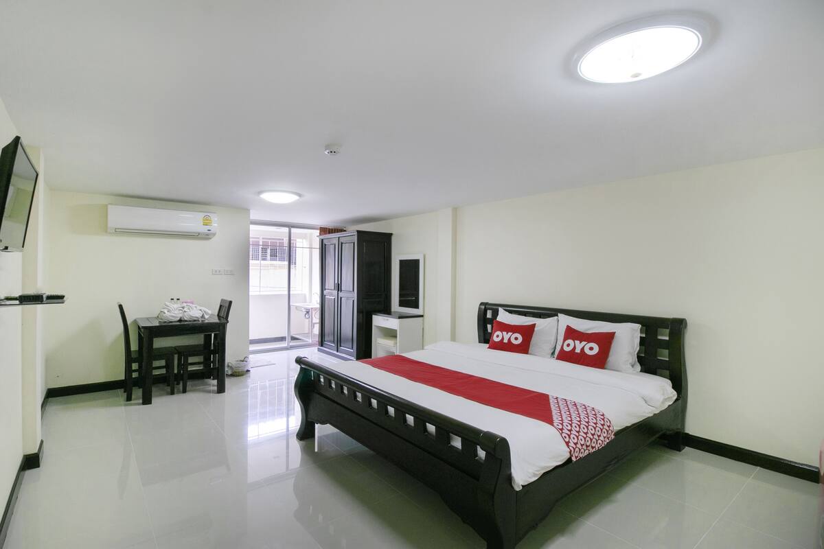 A hotel room with a bed, a desk, a chair, an air conditioning unit, and a television.