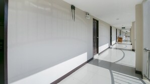 A long, narrow hallway with white walls and a tiled floor, leading to a set of doors at the end. - OYO 75390 Sunee Place Hotel (Ban Chang)