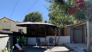 A patio with two chairs and a table under a large umbrella, surrounded by potted plants and a grassy area. - Shabby Chic Studio in LA Hills (Alhambra)