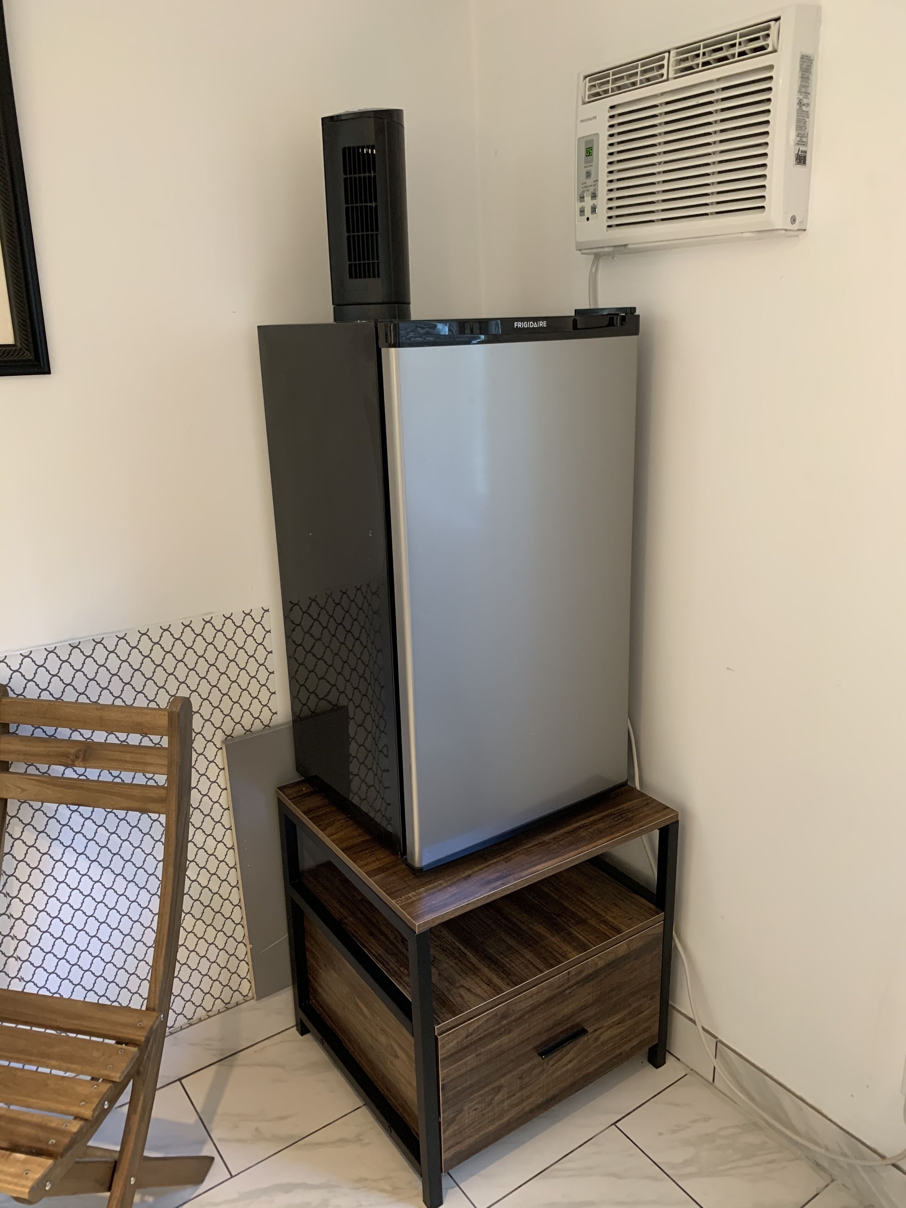 A corner of a room with a wooden chair, a tall black appliance, and a white wall-mounted unit.