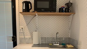 A kitchen with a microwave, coffee maker, and a shelf with a plant. There are two drawers and a sink with a faucet. - Shabby Chic Studio in LA Hills (Alhambra)