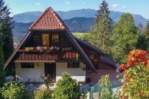 A traditional chalet with a sloped roof, wooden balcony, and a view of mountains.