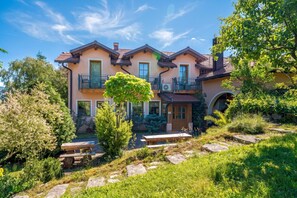 A two-story house with a balcony, a stone pathway, and a variety of greenery.