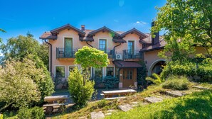 A multi-story house with a balcony, a garden with a bench, and a stone pathway.