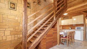 A wooden staircase leading to a kitchen area with stone walls and wooden cabinets.