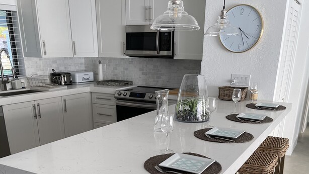 A modern kitchen with white cabinetry, a central island with bar stools, and a dining area set for four.