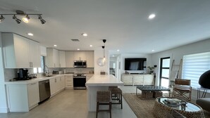 A modern kitchen with white cabinetry, a central island, and a dining area with a sofa and coffee table.