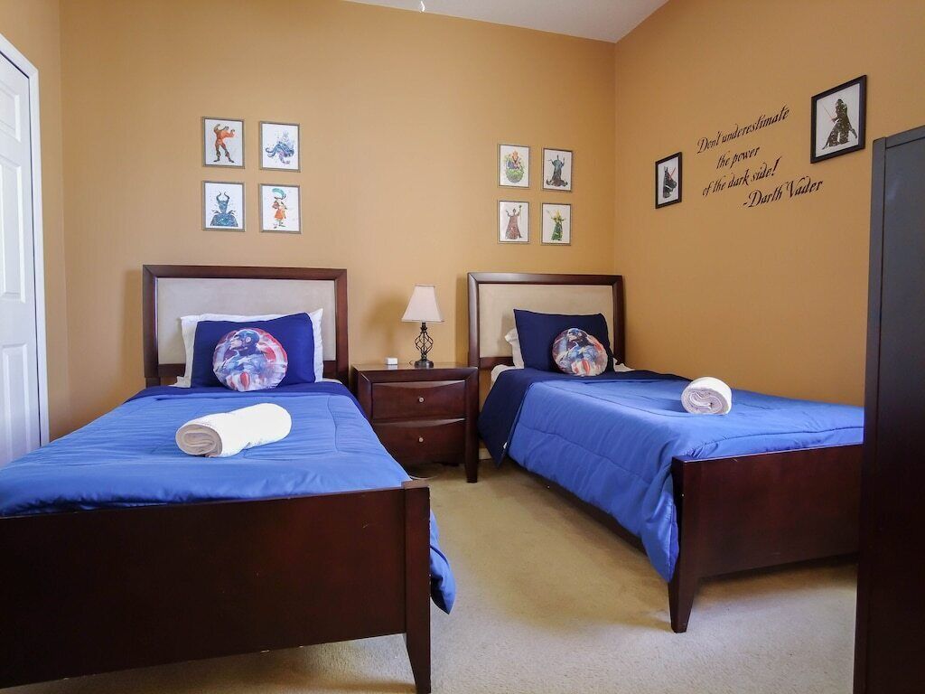 Ein Hotelzimmer mit zwei Betten, jeweils mit blauer Bettwäsche und dekorativen Kissen. An den Wänden befinden sich gerahmte Bilder und ein Zitat von Darth Vader.