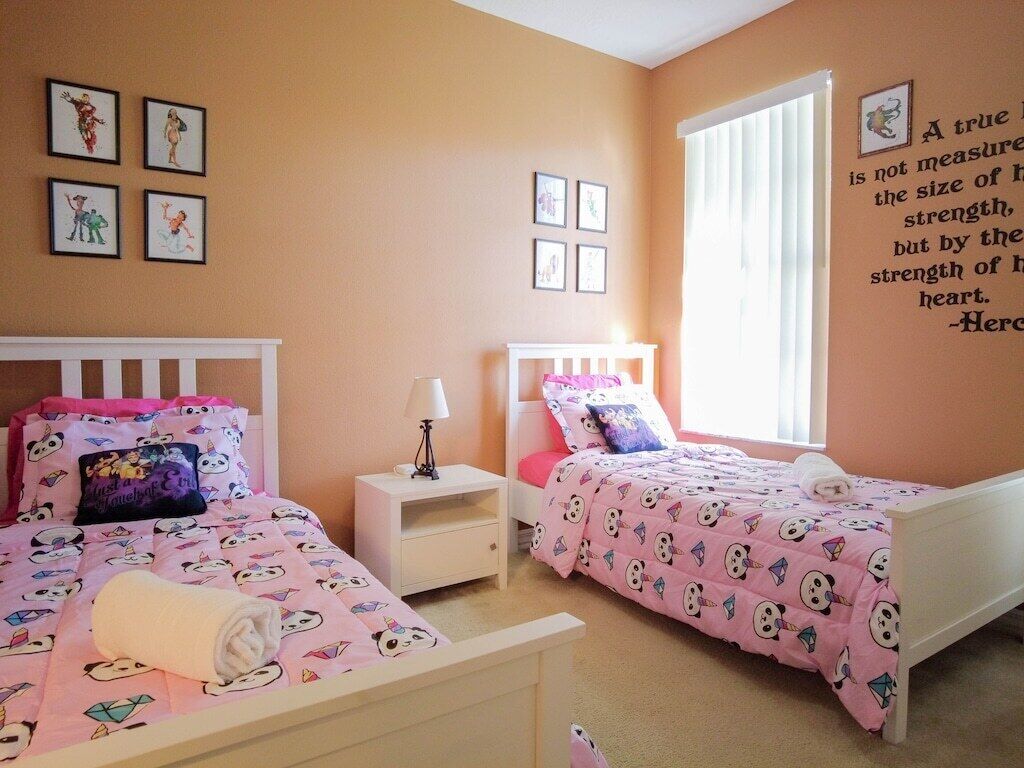 Een slaapkamer met twee bedden, elk met een roze dekbedovertrek met tekenfilmfiguren. Er hangen foto's aan de muur en staat een motiverende quote op de muur.