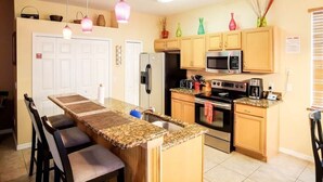 Una cocina con isla central, armarios de madera, microondas, estufa y refrigerador.
