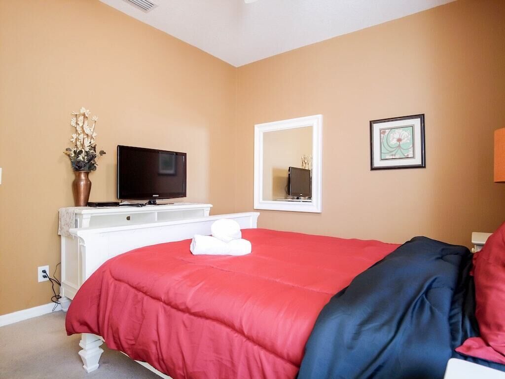 Une chambre à coucher avec un lit, une télévision, un miroir et un vase de fleurs.