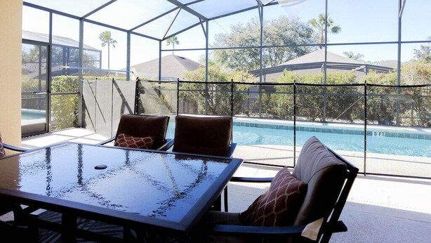 Un patio con paredes de vidrio y vista a la piscina, una mesa y sillas.