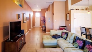 Una sala de estar con sofá modular, televisor y ventilador de techo.