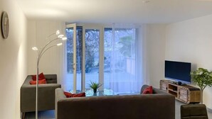 Una sala de estar moderna con un sofá, una lámpara de pie, un televisor y un ventanal corredera que da a un balcón.