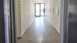 Un pasillo con paredes y piso de baldosas, que conduce a una puerta de cristal.